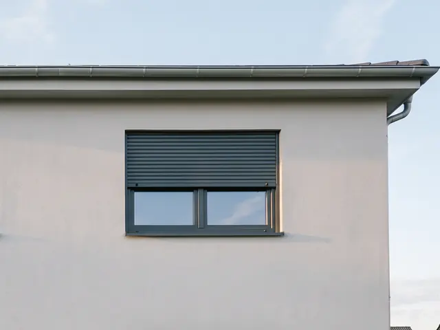 Anthrazitfarbenes Fenster mit halb heruntergelassenem Rollladen in einer hellen Putzfassade
